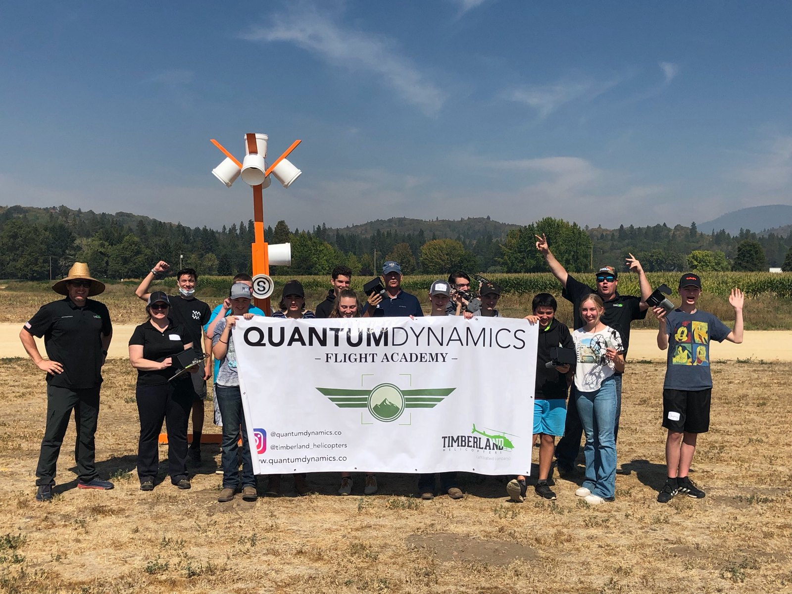 Quantum Dynamics Flight Academy youth STEM students and instructors holding the academy banner beside the segmented circle at the Oregon flight field, drones in hand